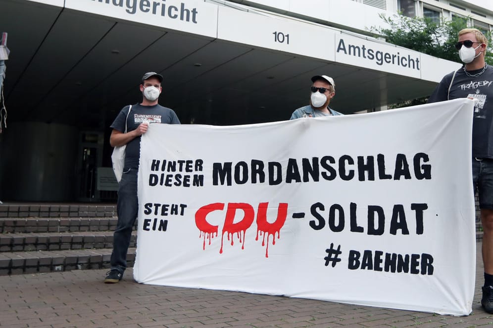 Drei Männer halten ein Banner vor dem Land-/Amtsgericht Köln bei einer Kundgebung zum Fall des ehemaligen Porzer CDU-Bezirksvertreters Hans-Josef Bähner: Der Prozess gegen den Politiker hat nach wie vor nicht begonnen.