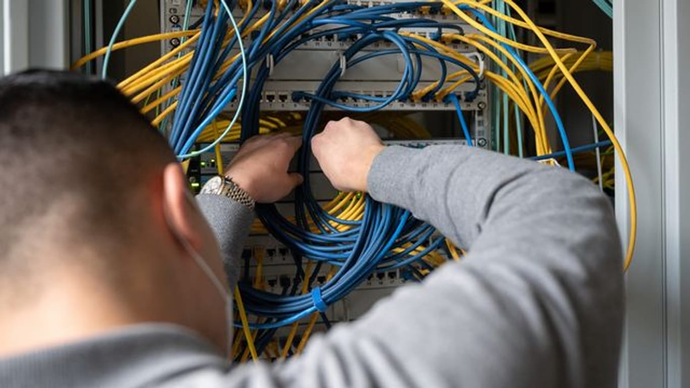 Ein Auszubildender Fachinformatiker steckt an einem Server ein Netzwerkkabel ein.
