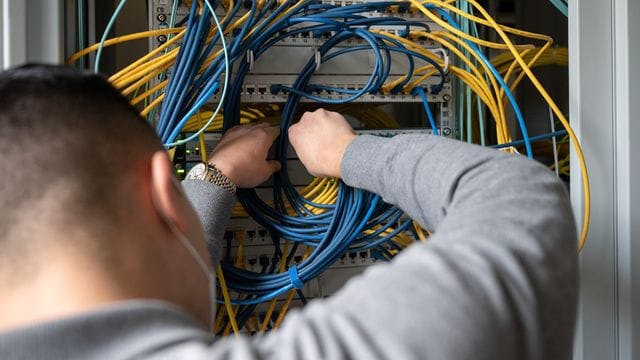 Ein Auszubildender Fachinformatiker steckt an einem Server ein Netzwerkkabel ein.