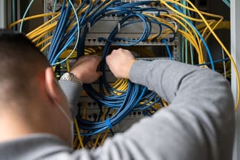 Ein Auszubildender Fachinformatiker steckt an einem Server ein Netzwerkkabel ein.