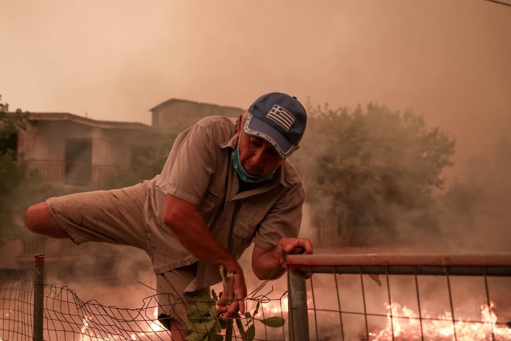 Ein Mann klettert während der Löscharbeiten auf der Insel Euböa über einen Zaun: Weiterhin sind viele Ortschaften von Flammen umzingelt.