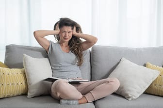 Eine junge Frau sitzt auf dem Sofa und hält sich die Ohren zu. Wenn die Freizeit mit Terminen "durchgetaktet" ist, entsteht negativer Stress.