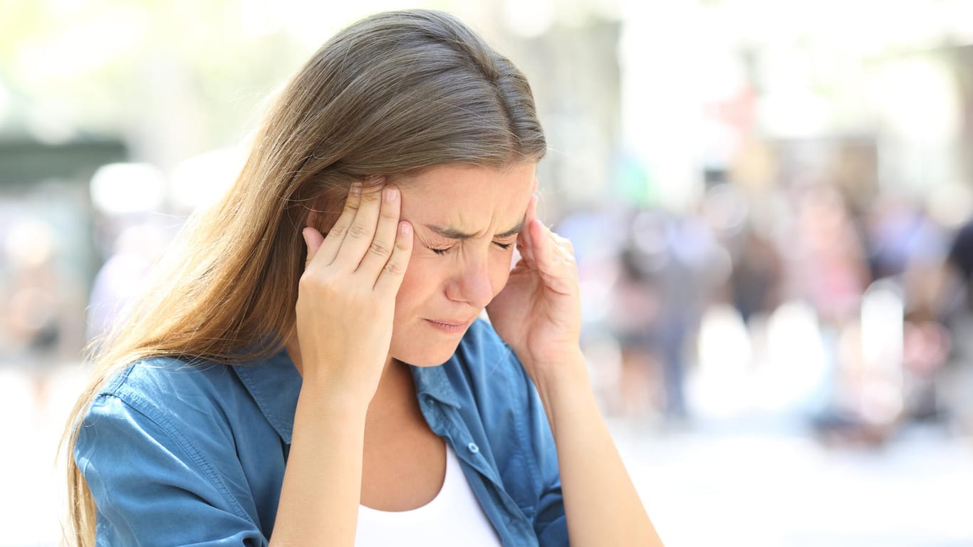 Eine junge Frau mit schmerzverzerrtem Gesicht greift sich an die Schläfen. Kopfschmerzen können ein Warnsignal für zu viel Stress sein.