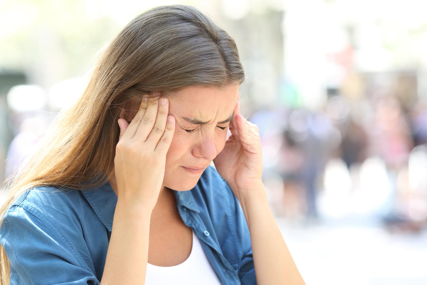 Eine junge Frau mit schmerzverzerrtem Gesicht greift sich an die Schläfen. Kopfschmerzen können ein Warnsignal für zu viel Stress sein.