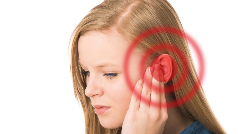 Eine junge Frau hält die linke Hand an ihr Ohr. Tinnitus kann viele Ursachen haben und verschwinden häufig von selbst. Halten sie Ohrgeräusche jedoch länger als 48 Stunden an, sollte man einen Arzt aufsuchen.