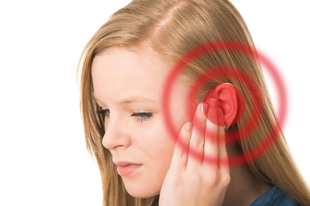 Eine junge Frau hält die linke Hand an ihr Ohr. Tinnitus kann viele Ursachen haben und verschwinden häufig von selbst. Halten sie Ohrgeräusche jedoch länger als 48 Stunden an, sollte man einen Arzt aufsuchen.