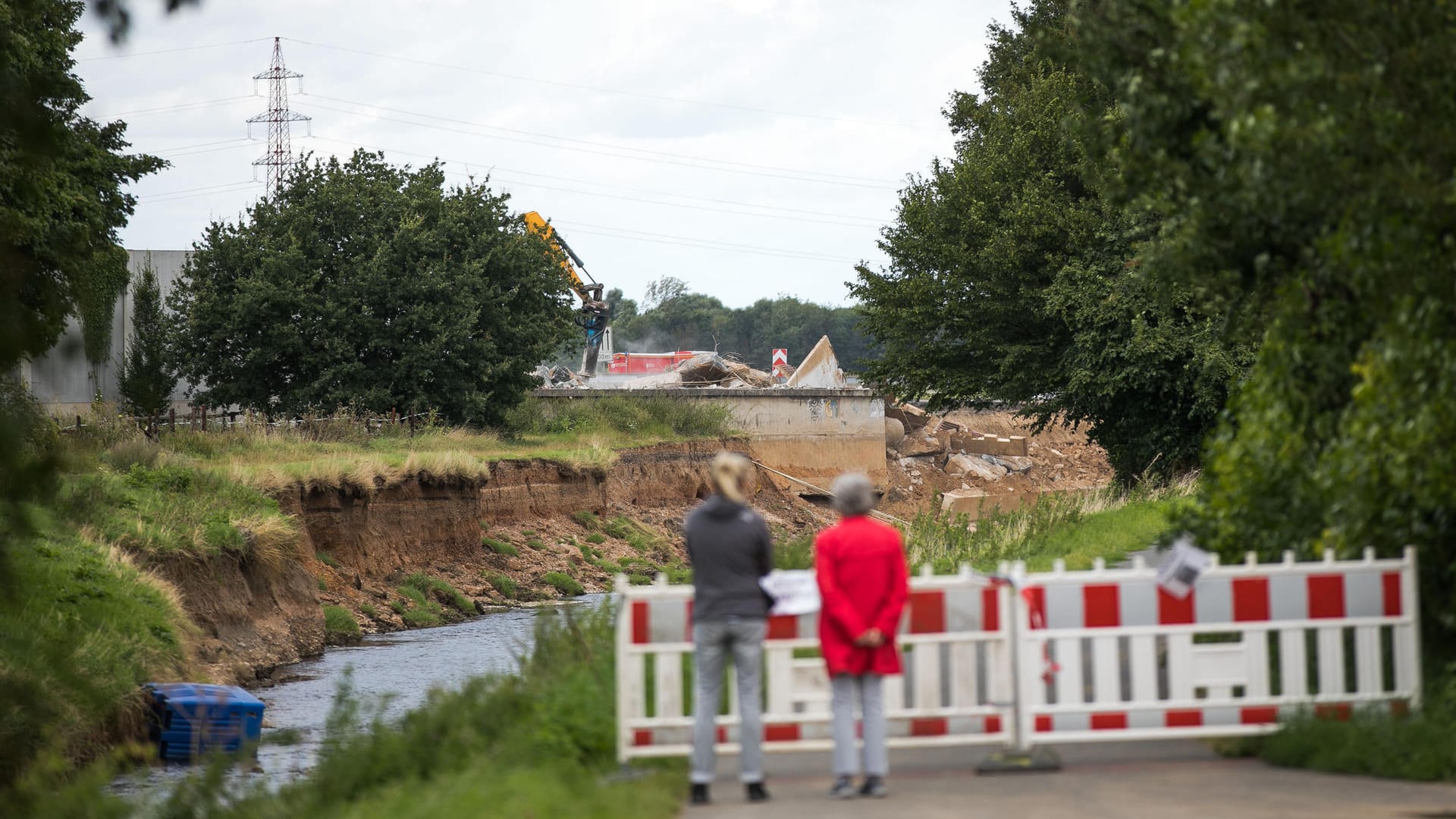 Zwei Passantinnen schauen auf den Flusslauf der Erft: Im Hintergrund sieht man die unterspülte Autobahn A61.