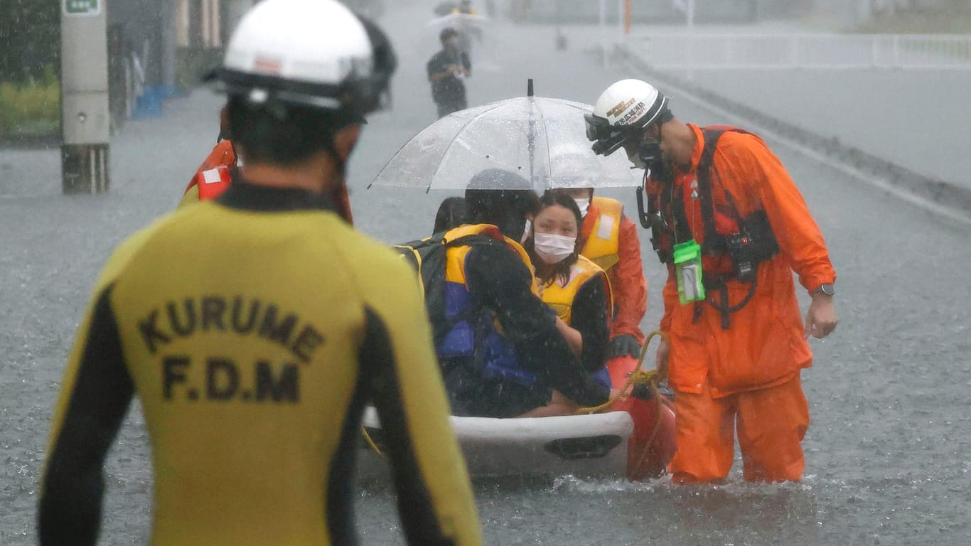 Gestrandete Anwohner auf einem Boot in einer von Regen überfluteten Straße im japanischen Kurume: Die höchste Alarmstufe müsse inzwischen schon in solchen Gebieten ausgelöst werden, in denen die Gefahr von Erdrutschen und Überschwemmungen "sonst nicht so hoch" sei, so ein Experte.