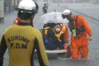 Gestrandete Anwohner auf einem Boot in einer von Regen überfluteten Straße im japanischen Kurume: Die höchste Alarmstufe müsse inzwischen schon in solchen Gebieten ausgelöst werden, in denen die Gefahr von Erdrutschen und Überschwemmungen "sonst nicht so hoch" sei, so ein Experte.