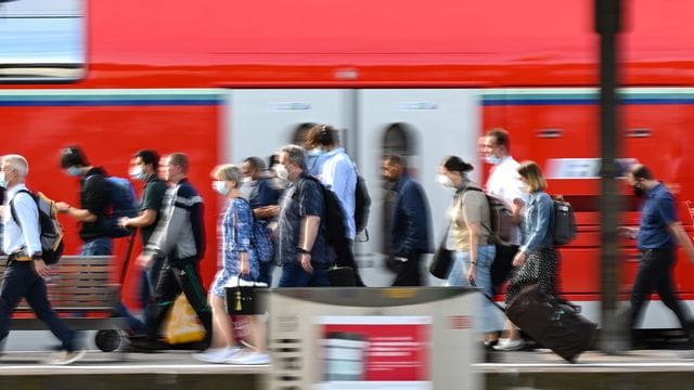 Passagiere gehen an einem Bahnhof an einem Regionalzug vorbei