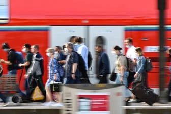 Passagiere gehen an einem Bahnhof an einem Regionalzug vorbei