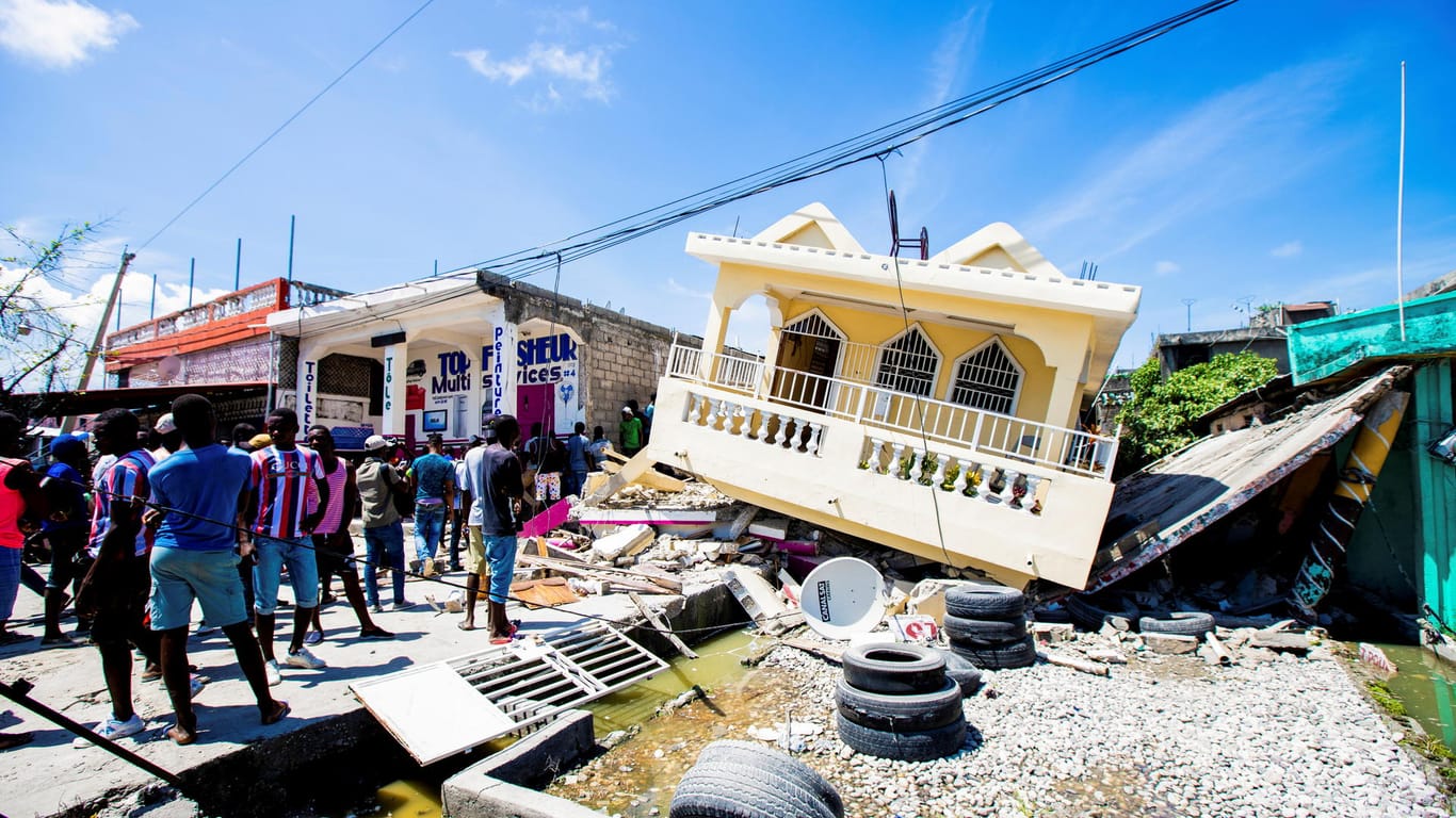 Menschen stehen vor einem vom Erdbeben zerstörten Haus in Les Cayes. Hunderte sind getötet worden.