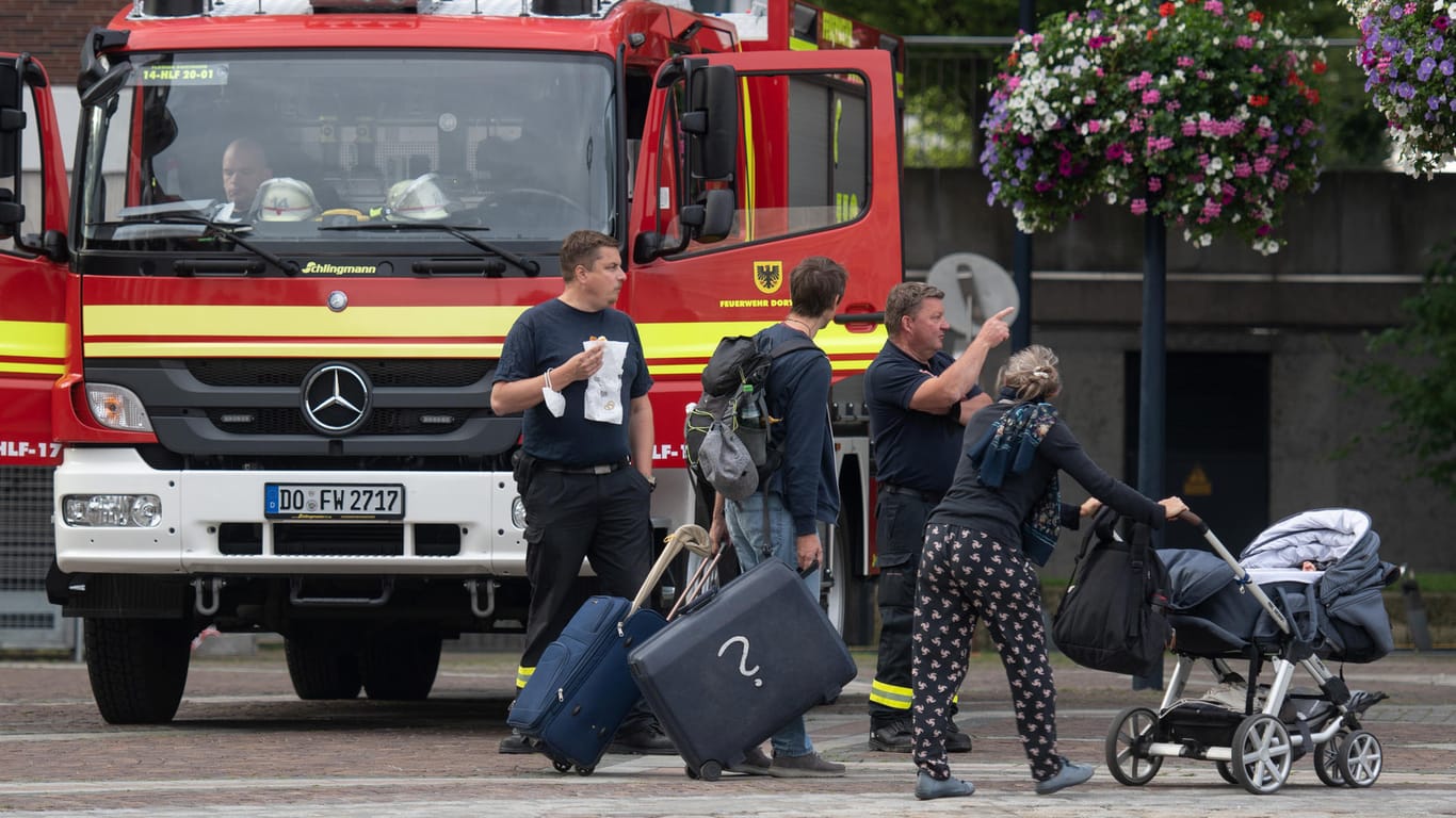 Ein Mann mit Koffern und eine Frau mit Kinderwagen gehen an einem Einsatzwagen der Feuerwehr vorbei: Wegen des Bombenfunds mussten Tausende ihre Wohnungen verlassen.
