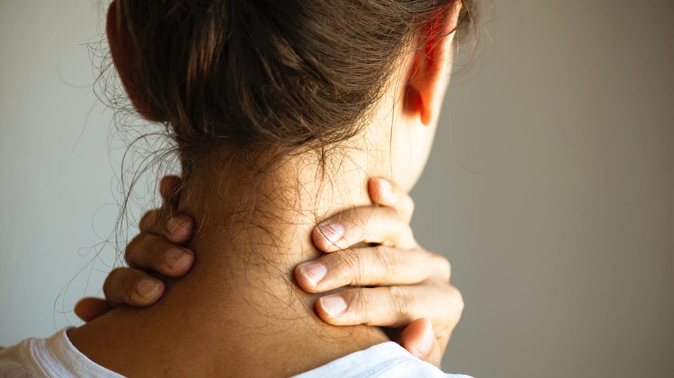 Eine Frau fasst sich an den Nacken. Muskelverspannungen im Nackenbereich können sehr schmerzhaft sein. Verursacht werden sie häufig durch Stress.