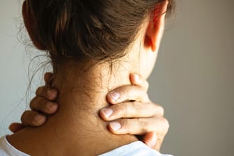 Eine Frau fasst sich an den Nacken. Muskelverspannungen im Nackenbereich können sehr schmerzhaft sein. Verursacht werden sie häufig durch Stress.