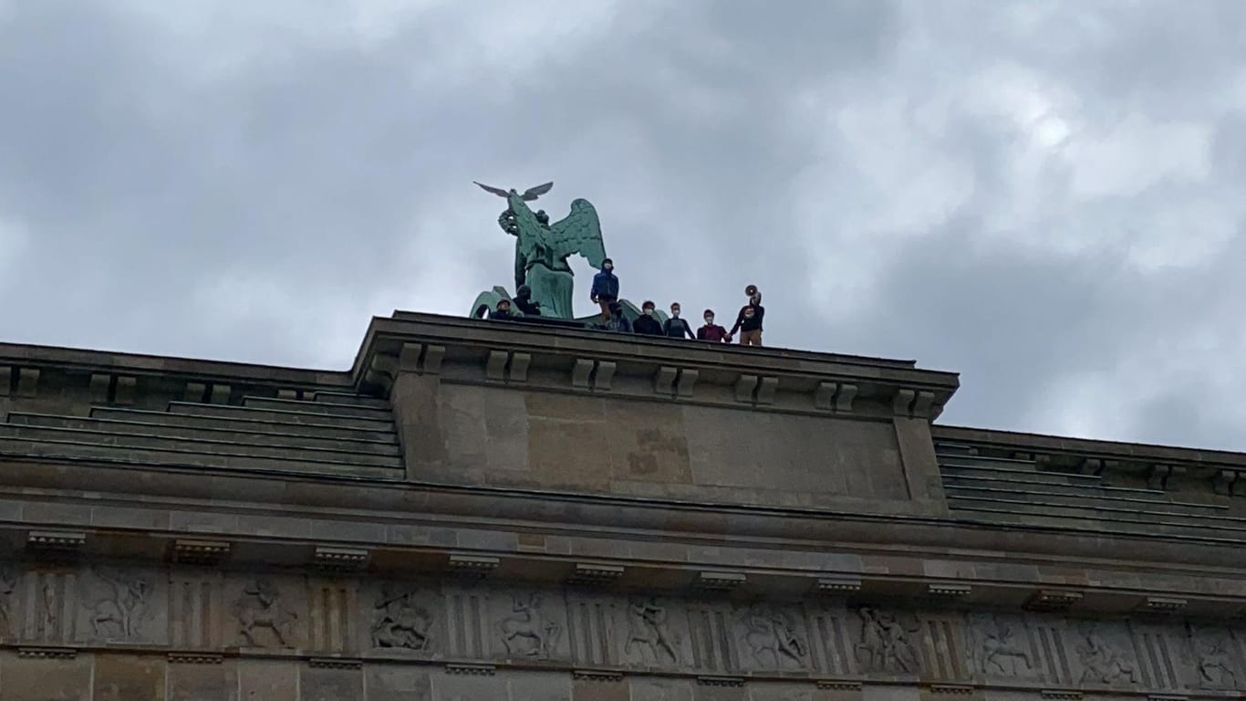 Personen stehen mit Megafon auf dem Brandenburger Tor: Auch Polizisten sind auf das Berliner Wahrzeichen geklettert, haben die Aktivisten aber noch nicht nach unten gebracht.