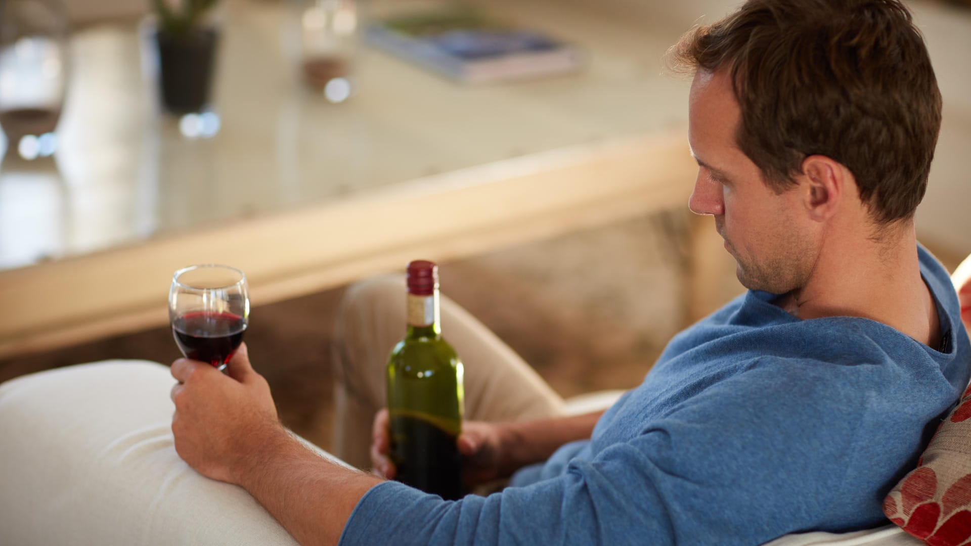 Ein Mann sitzt allein mit Wein auf dem Sofa: Menschen, die an Alkoholismus leiden, verheimlichen ihre Sucht vor anderen.