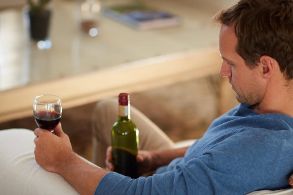 Ein Mann sitzt allein mit Wein auf dem Sofa: Menschen, die an Alkoholismus leiden, verheimlichen ihre Sucht vor anderen.