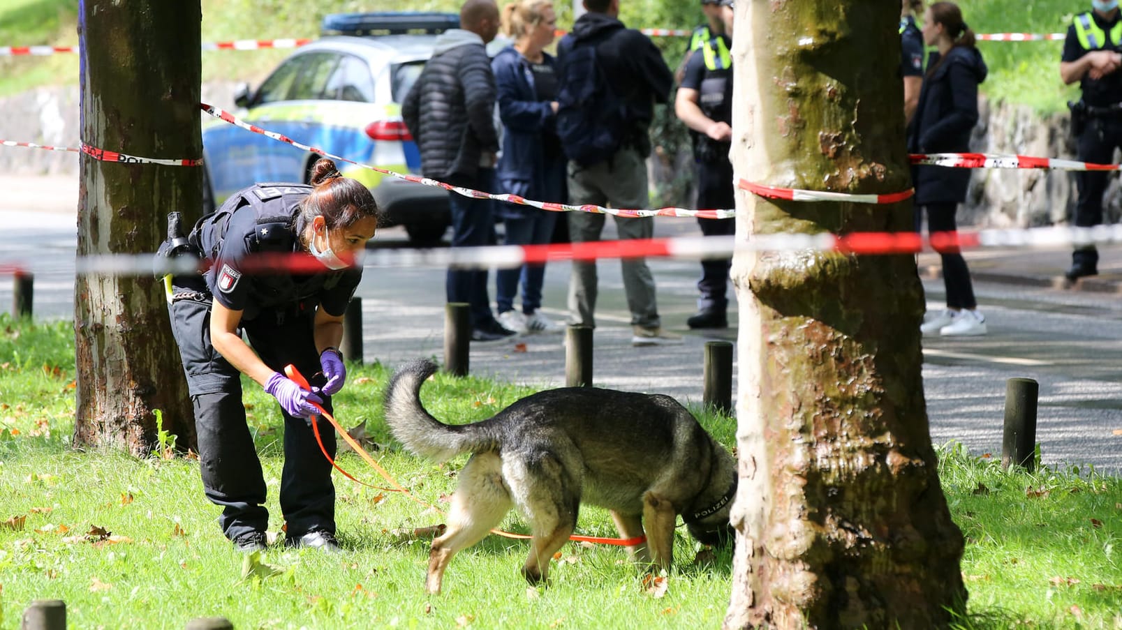 Eine Polizistin ist innerhalb einer Polizeiabsperrung mit einem Spürhund im Einsatz: Die Hintergründe der Tat sind noch unklar.