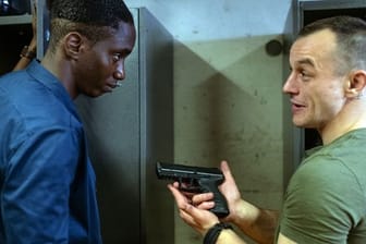 Mario (Paul Wollin, r) prahlt vor seinem Kollegen Man (Emmanuel Ajayi) mit seiner Pistole.