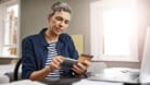 Ältere Frau mit Unterlagen und Smartphone (Symbolbild): Rentenpunkte kaufen, um Abschläge auszugleichen, kann man nach Vollendung des 50. Lebensjahres.