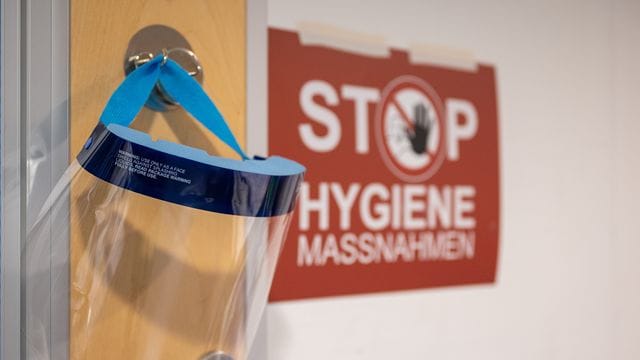 Ein Gesichtsschutz hängt neben einem Schild mit der Aufschrift "Stop Hygienemaßnahmen" (Symbolbild): Für Ungeimpfte könnte es wieder zu Kontaktbeschränkungen kommen.