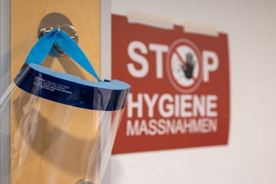 Ein Gesichtsschutz hängt neben einem Schild mit der Aufschrift "Stop Hygienemaßnahmen" (Symbolbild): Für Ungeimpfte könnte es wieder zu Kontaktbeschränkungen kommen.