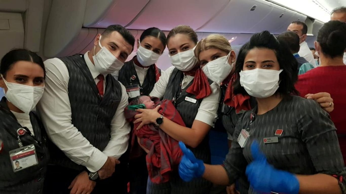 Besatzungsmitglieder haben sich zum Bild mit dem Neugeborenen versammelt. Das Kind kam mitten im Flug zur Welt.