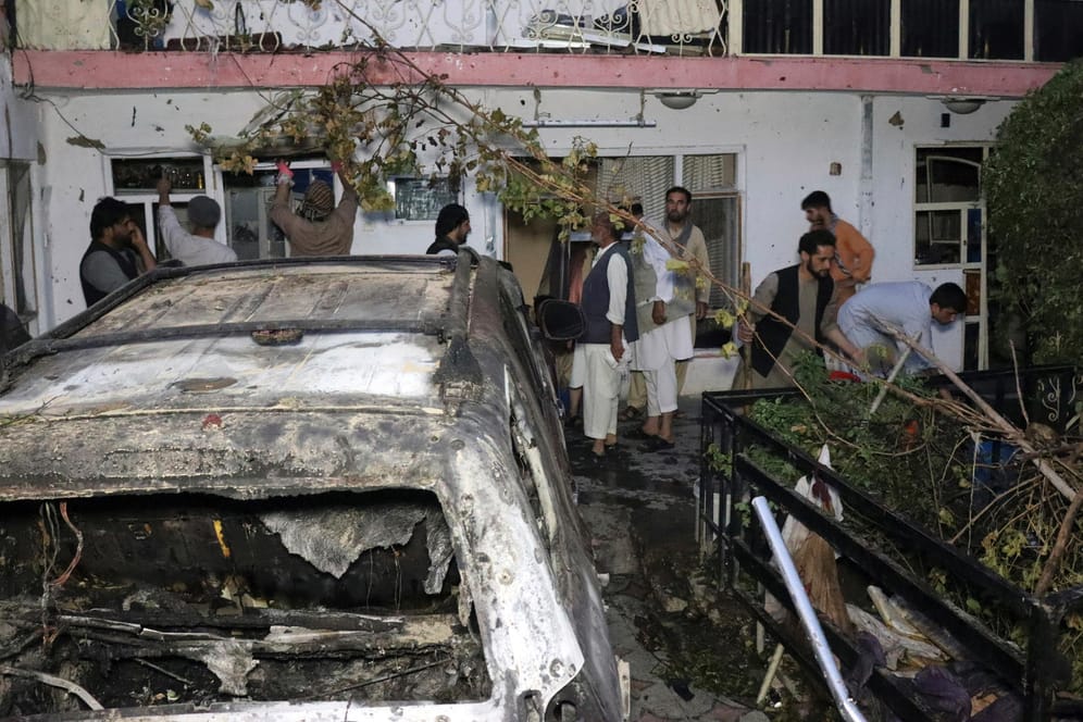 Afghanische Bürger stehen um ein ausgebranntes Fahrzeug. Es soll nach US-Angaben Sprengstoff geladen haben. Berichte über zivile Opfer werden geprüft.
