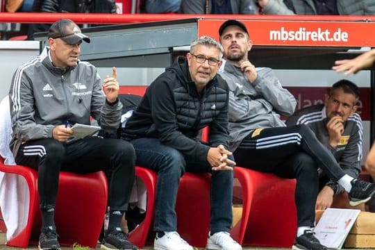 Unions Co-Trainer Markus Hoffmann, Trainer Urs Fischer und Co-Trainer Sebastian Bönig (l-r) sitzen auf Bank.
