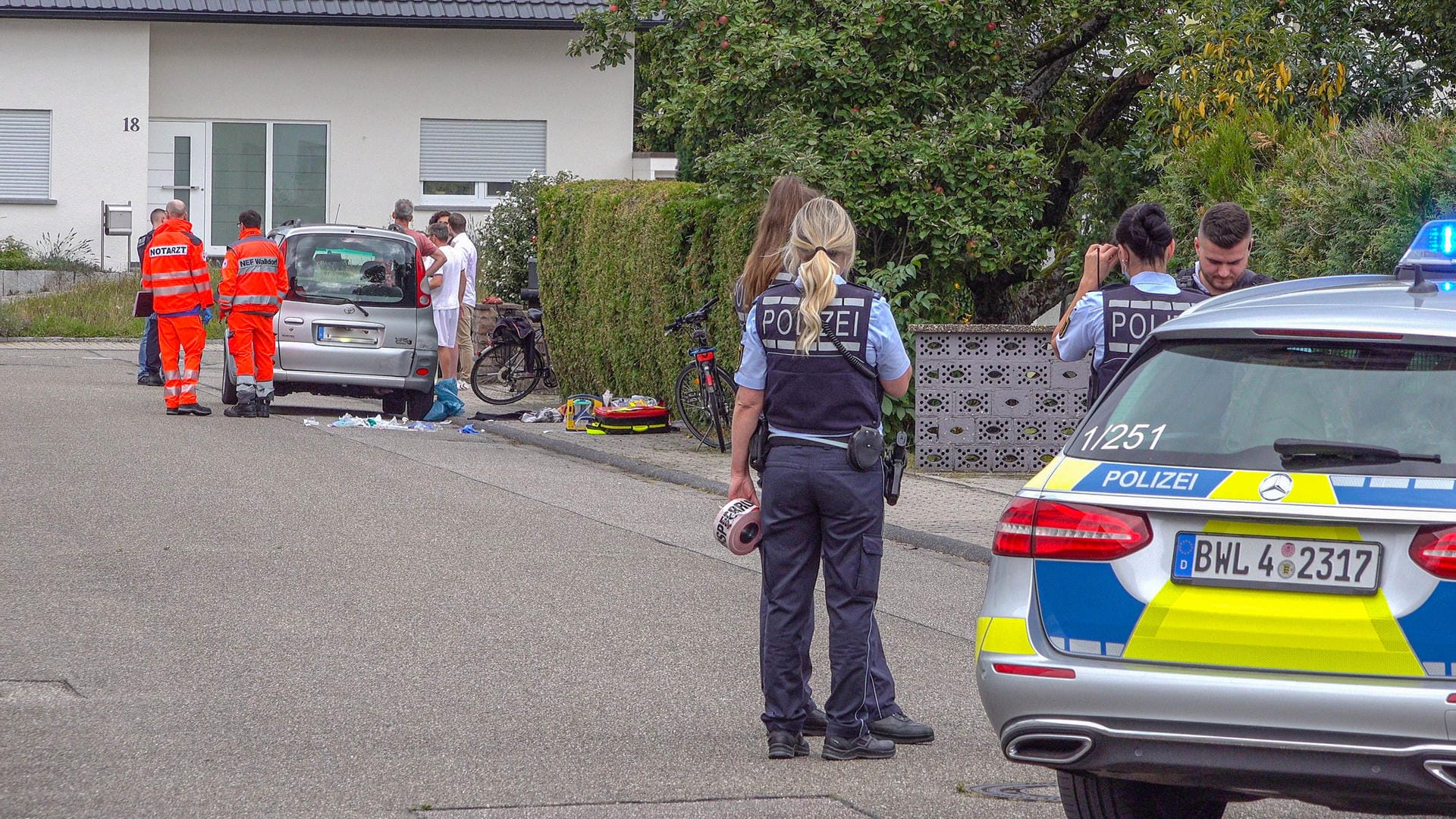 Polizisten sperren eine Straße ab, in der Rettungssanitäter neben einem PKW stehen: Bei einem Streit zwischen zwei Brüdern ist einer der beiden tödlich verletzt worden.