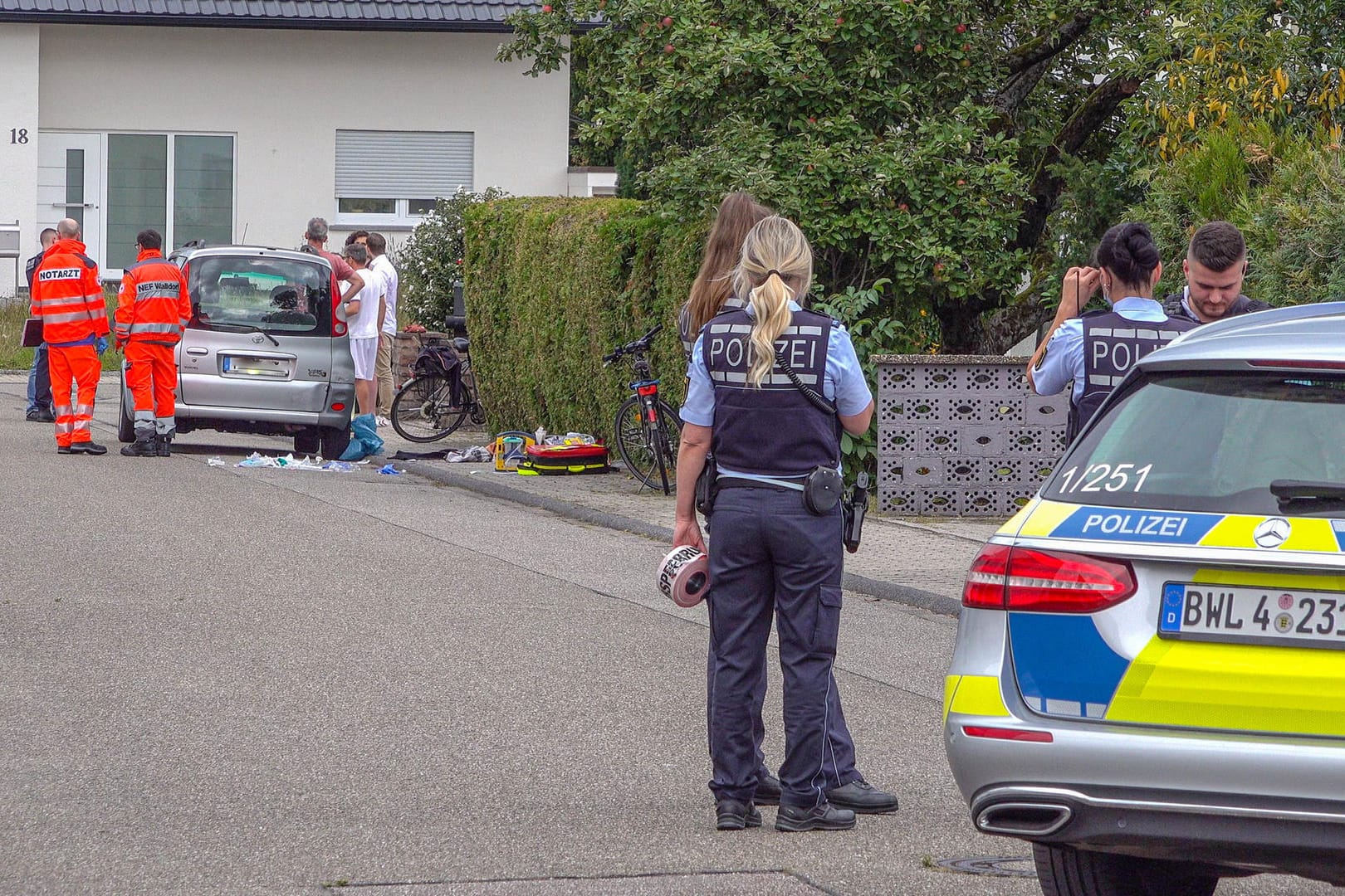 Polizisten sperren eine Straße ab, in der Rettungssanitäter neben einem PKW stehen: Bei einem Streit zwischen zwei Brüdern ist einer der beiden tödlich verletzt worden.