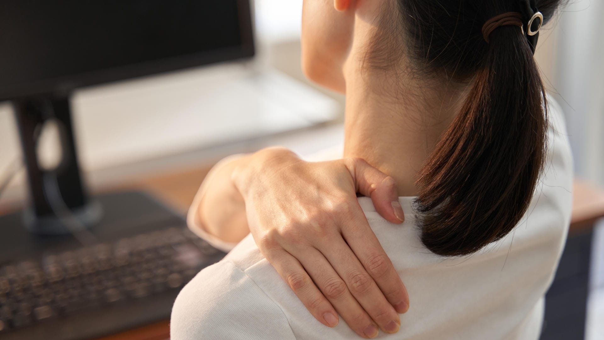 Eine Frau sitzt am Computer und greift sich an die verspannte Schulter. Für viele Beschäftige ist durch das Homeoffice der Stresspegel gestiegen.