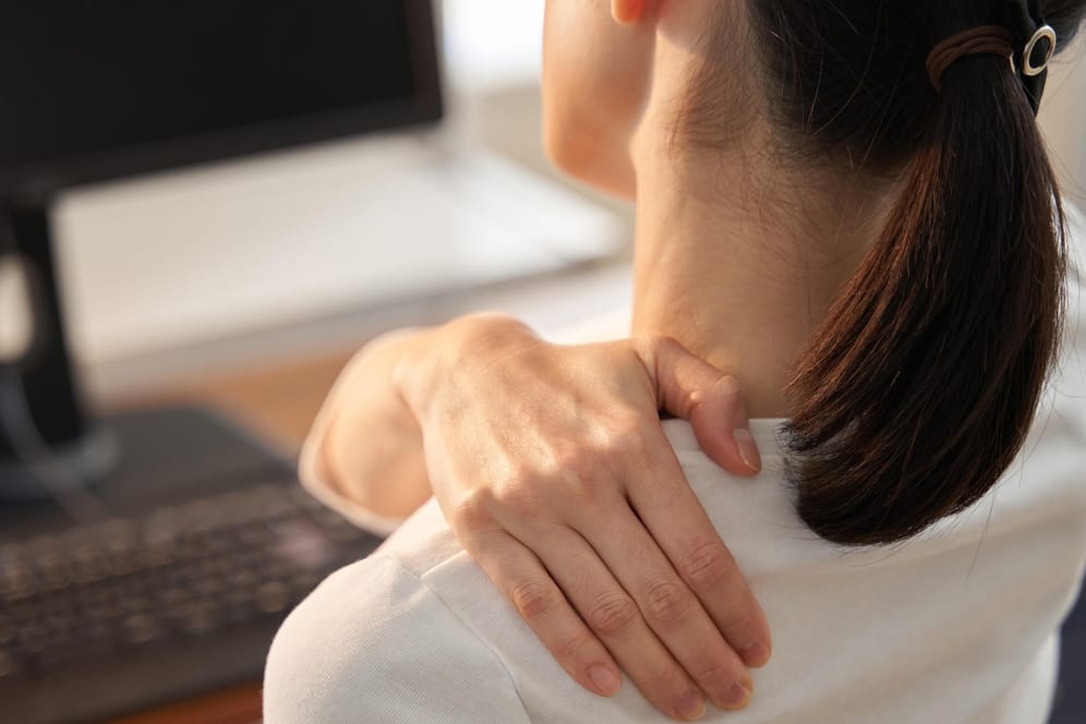 Eine Frau sitzt am Computer und greift sich an die verspannte Schulter. Für viele Beschäftige ist durch das Homeoffice der Stresspegel gestiegen.