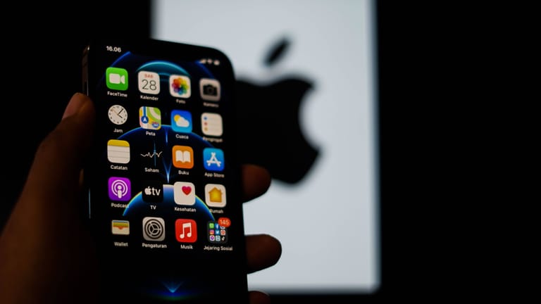 Jemand hält ein iPhone in der Hand und im Hintergrund ist das Apple-Logo.