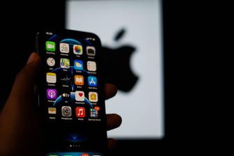 Jemand hält ein iPhone in der Hand und im Hintergrund ist das Apple-Logo.