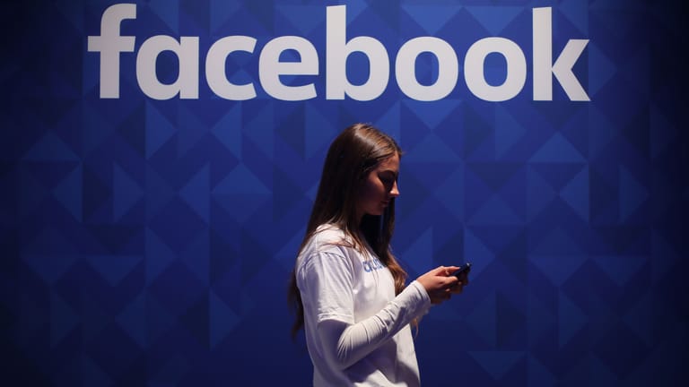 Ein Frau vor Facebook-Logo (Symbolbild): US-Kartellwächter ziehen erneut gegen Facebook vor Gericht.