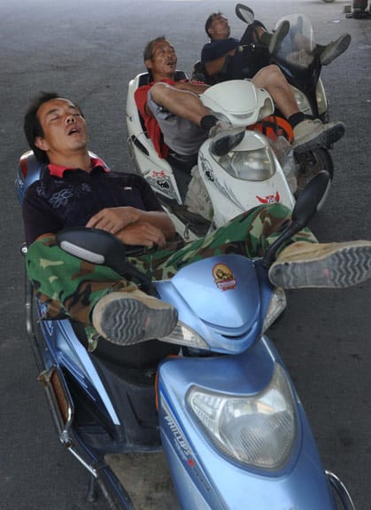 Drei Wanderarbeiter aus China schlafen auf ihren Motorrollern. Drei Wanderarbeiter aus China schlafen auf ihren Motorrollern.