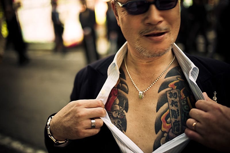 Ein Straßenkämpfer der Yakuza zeigt mit aggressivem Stolz den Beweis seiner Mitgliedschaft: Ein großflächiges Tattoo. Ein Straßenkämpfer der Yakuza zeigt mit aggressivem Stolz den Beweis seiner Mitgliedschaft: Ein großflächiges Tattoo.