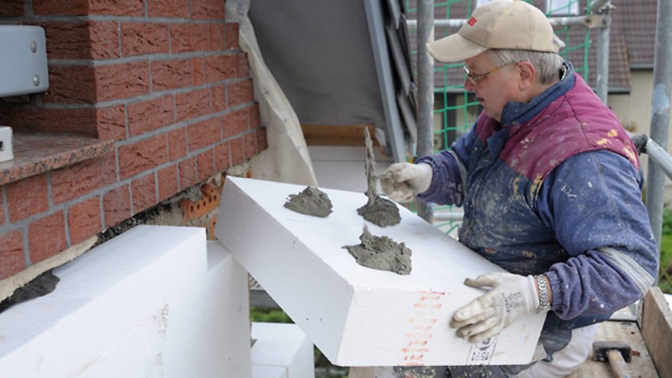 Ein Maler klebt Styropor-Fassadendämmplatten an ein Haus