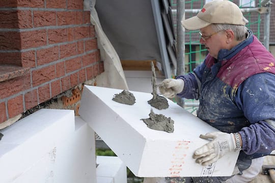 Ein Maler klebt Styropor-Fassadendämmplatten an ein Haus