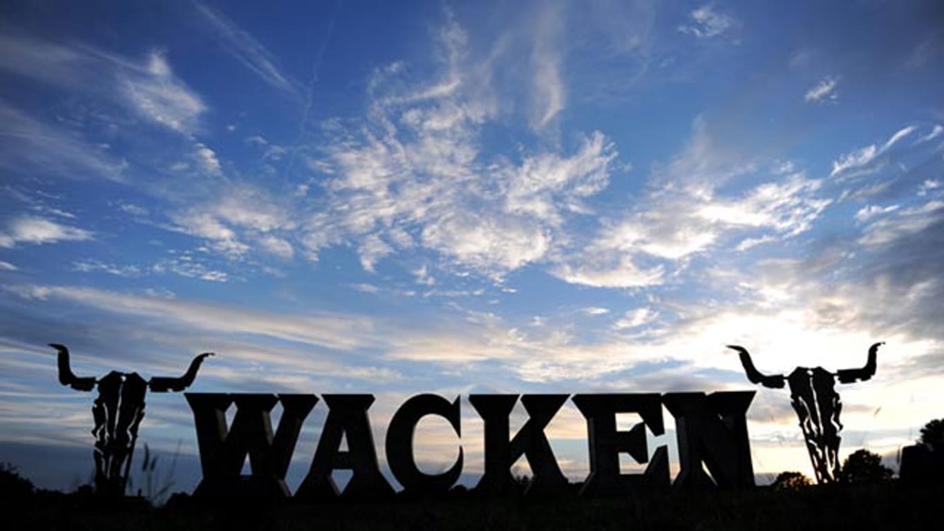 Der Wacken Schriftzug hebt sich vor dem Gelände vom Wacken Open Air Festival vor blauem Himmel ab.