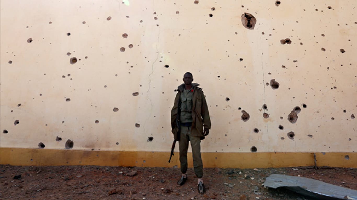 Ein Soldat steht in Konna vor einer von Kugeln und Bombensplittern durchlöcherten Wand.