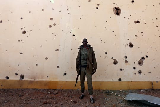Ein Soldat steht in Konna vor einer von Kugeln und Bombensplittern durchlöcherten Wand.