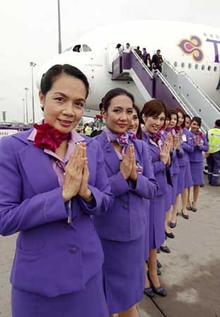 Thai Airways: Bei den Uniformen der Stewardessen dominieren Orchideen-Farben. Passend zum lila Kostüm werden hochhackige, lila Schuhe getragen. Als Accessoires dienen flieder-, und purpurfarbene Halstücher.