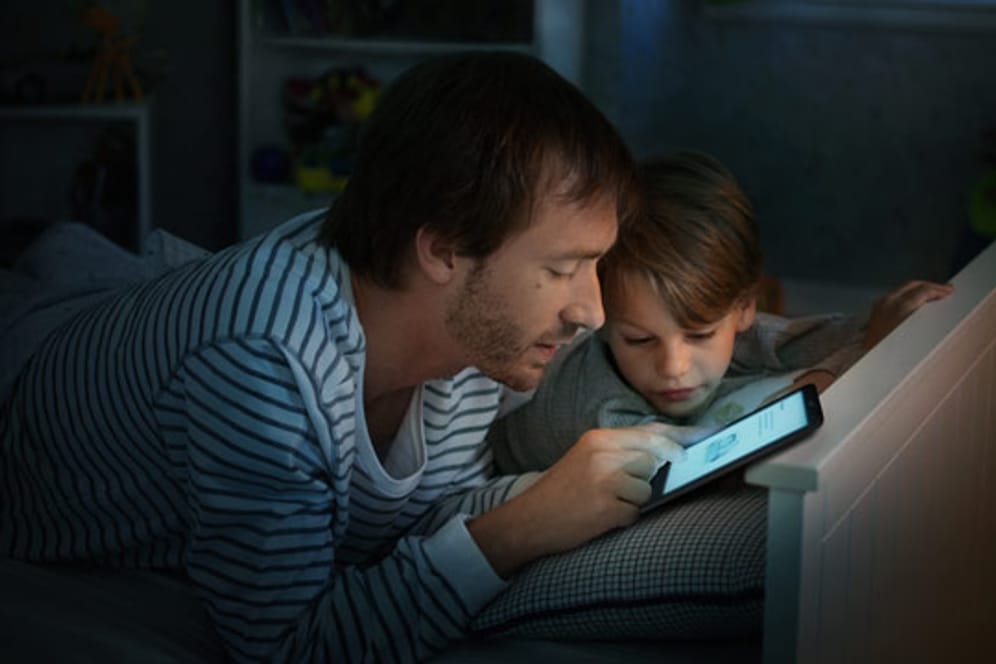 Vater liest Sohn mit einem tolino E-Book-Reader vor.