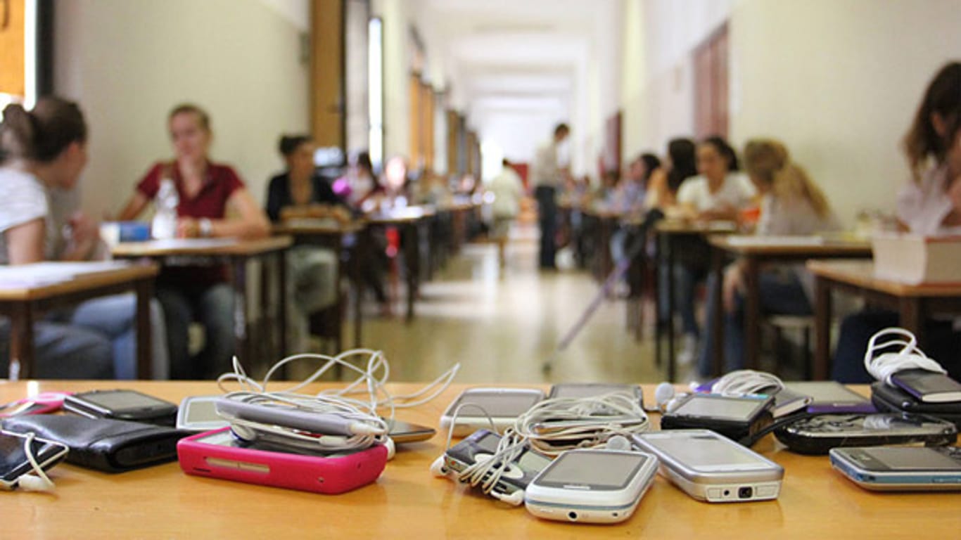 Bei einer Abiturprüfung liegen die Handys der Schüler auf dem Lehrerpult.