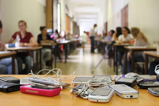 Bei einer Abiturprüfung liegen die Handys der Schüler auf dem Lehrerpult.