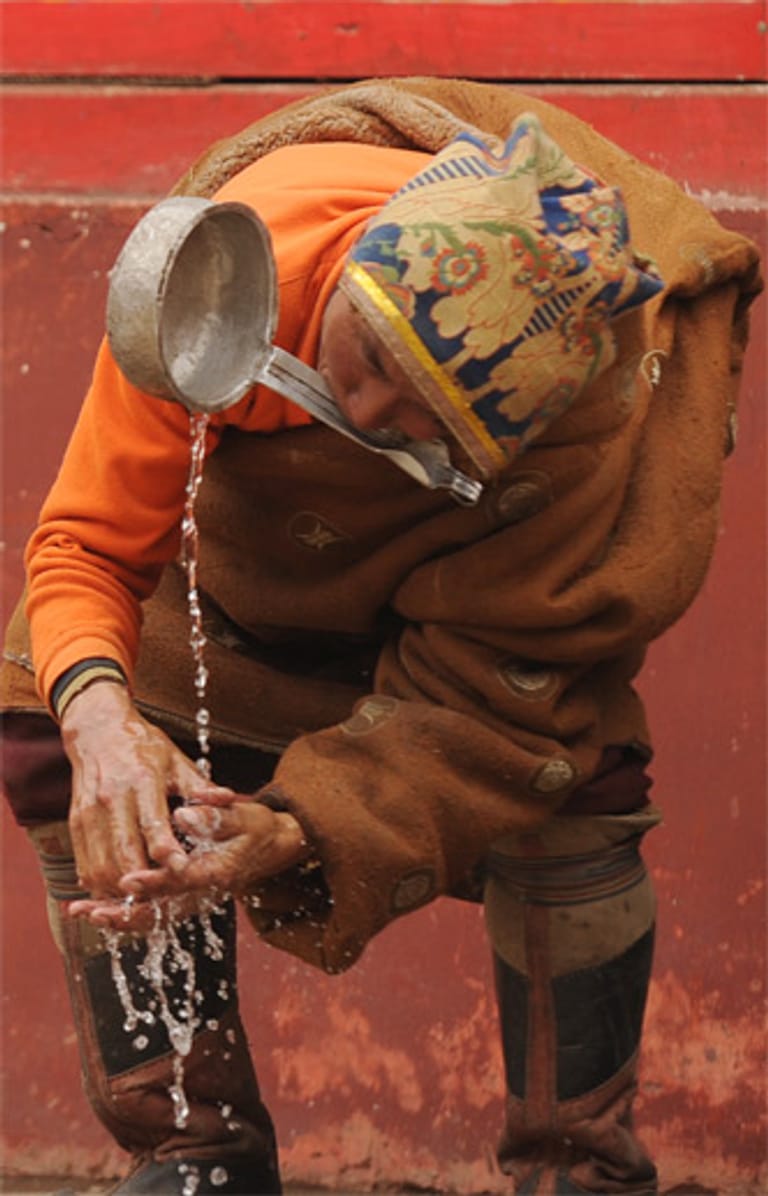 Geschickt wäscht sich ein Tibeter im Kloster seine Hände mit einer Schöpfkelle.