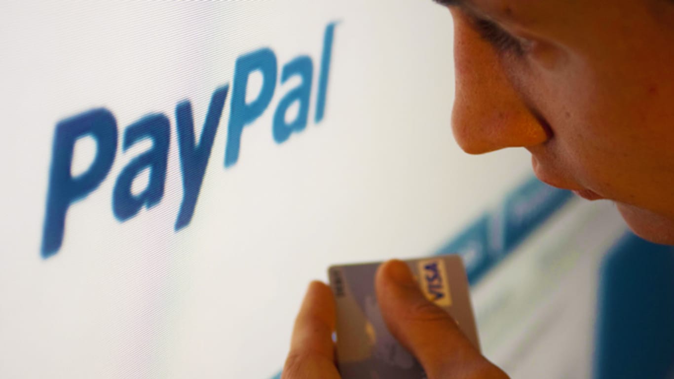 Mann hält Bankkarte in der Hand und schaut auf Paypal-Konto